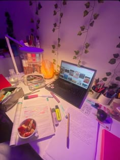 a laptop computer sitting on top of a desk next to a bowl of fruit and writing utensils