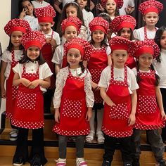 a group of children in red aprons and hats posing for a photo with their teacher