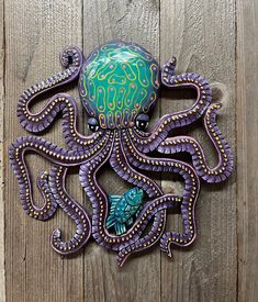 an octopus sculpture is hanging on the side of a wooden wall with purple and green decorations