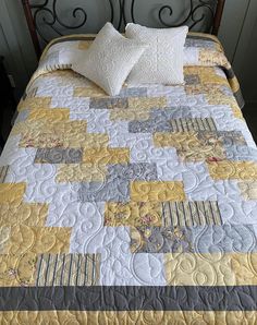 a bed with yellow and gray quilts on it's headboard next to a night stand