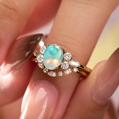 a woman's hand holding a ring with an opal and diamonds on it