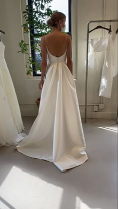 a woman standing in front of a window wearing a wedding dress with a bow on the back