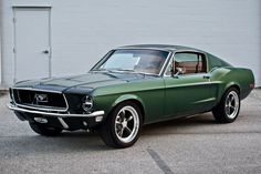 a green mustang parked in front of a garage