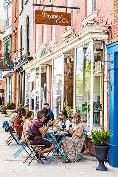 people are sitting at tables outside in front of stores on the sidewalk, eating and drinking