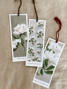 two cards with white flowers on them are hanging from twine strings, next to each other