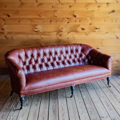 a brown leather couch sitting on top of a wooden floor next to a wood wall