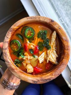 a person holding a wooden bowl filled with soup and veggies on top of it