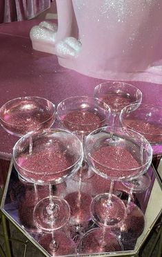 there are many wine glasses that are on the glass table and one is filled with pink liquid