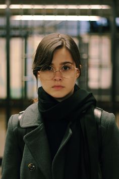 a woman wearing glasses standing in front of a building with a black scarf around her neck