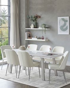 a dining room table with white chairs in front of a gray wall and shelves above it