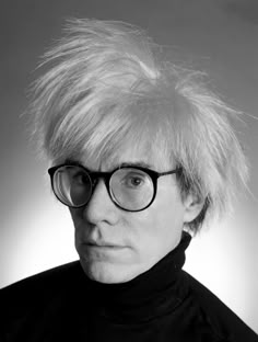 a black and white photo of a person wearing glasses with blonde hair in front of a gray background