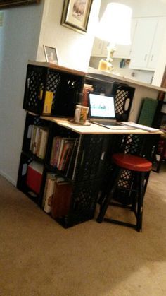 a computer desk sitting in the middle of a living room next to a book shelf