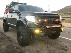 a black toyota truck is parked on the side of the road with its lights on