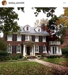 a large brick house with black shutters and white trim on the front door is surrounded by fall foliage