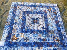 a blue and white quilt is laying on the ground with grass in front of it