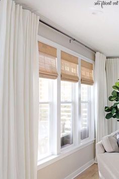 a living room with white drapes and curtains on the windowsills, in front of a large potted plant