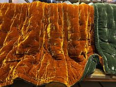 an orange and green blanket sitting on top of a wooden table next to other blankets