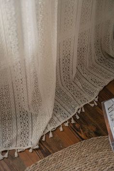 an open book sitting on top of a wooden floor next to a white lace curtain