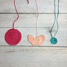 three crocheted ornaments hanging from strings on a white wooden surface, one is pink and the other is blue