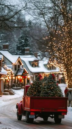 a red truck with a christmas tree in the back driving down a snow covered street