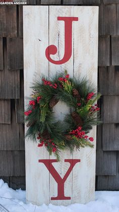 a wooden sign that says joy with wreaths and pine cones on the front door