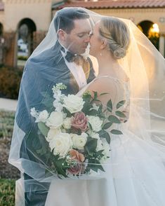 a bride and groom kissing under a veil on their wedding day in front of a building