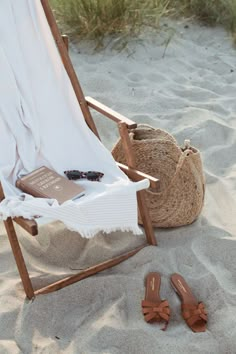 a beach chair on the sand with a book and some sandals laying next to it