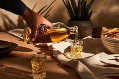 a person pouring whiskey into two glasses on a table