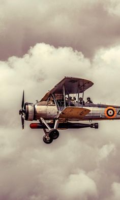 an old fashioned airplane flying in the sky with clouds behind it and people on top