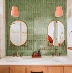 two sinks in a bathroom with green tiles on the wall and gold trim around them