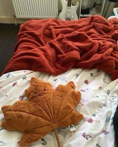 a teddy bear laying on top of a bed next to an orange leaf shaped pillow