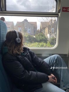 a woman sitting on a train with headphones in her ears looking out the window