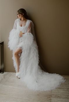 a woman in a white dress is leaning against a wall and holding a cup with her legs