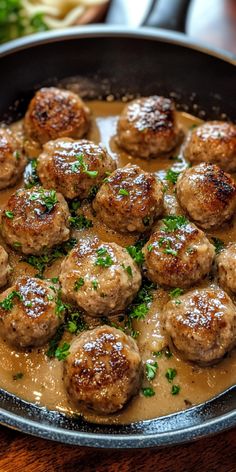 meatballs and gravy in a skillet on a wooden table with parsley