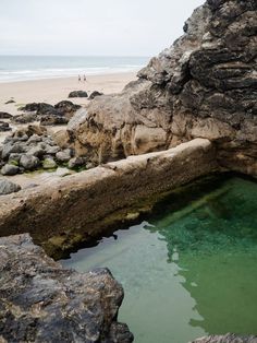 the water is clear and green in this rocky beach area with people walking on the shore