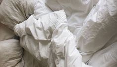 an unmade bed with white sheets and pillows