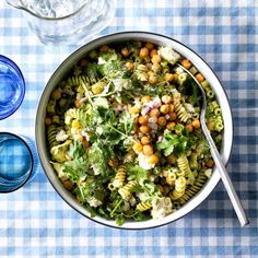 a white bowl filled with pasta salad next to two water glasses on a blue and white checkered table cloth