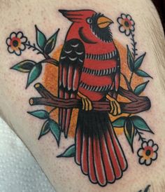 a red bird sitting on top of a tree branch with leaves and flowers around it