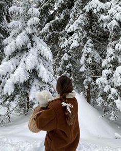 a woman walking through the snow carrying a white dog on her back and trees in the background