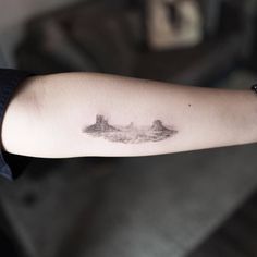 a person's arm with a small tattoo on it that has mountains in the background