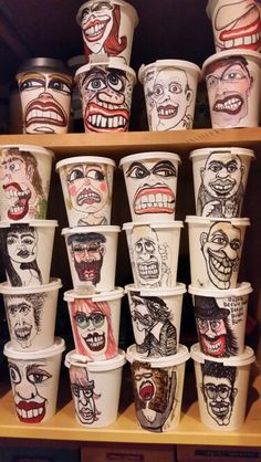 many cups with faces painted on them are stacked up in a shelf next to each other