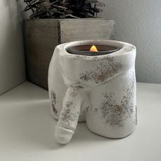 a white candle holder sitting on top of a table next to a box with a christmas tree in it