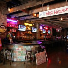 the inside of a bar with neon signs on the wall and stools in front of it