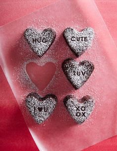 four heart shaped cookies with the words cute on them sitting on a pink napkin next to some sugar sprinkles