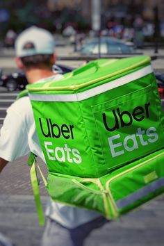 a man walking down the street carrying a large green bag with words on it that read upper eats eats