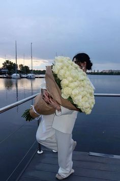 a woman holding a bouquet of flowers on top of a boat dock next to the water