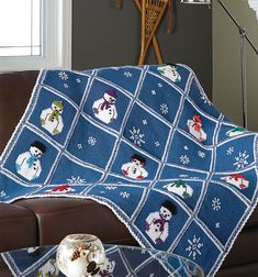 a blue blanket with snowmen on it sitting next to a brown leather couch and coffee table