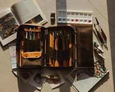 an open leather case sitting on top of a table filled with art supplies