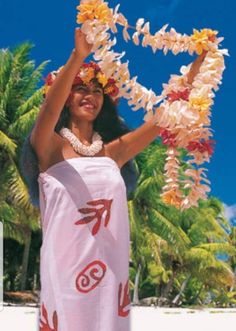 a woman in a hula skirt on the beach with flowers around her neck and head