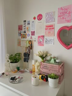 a white desk topped with lots of clutter next to a wall covered in pictures